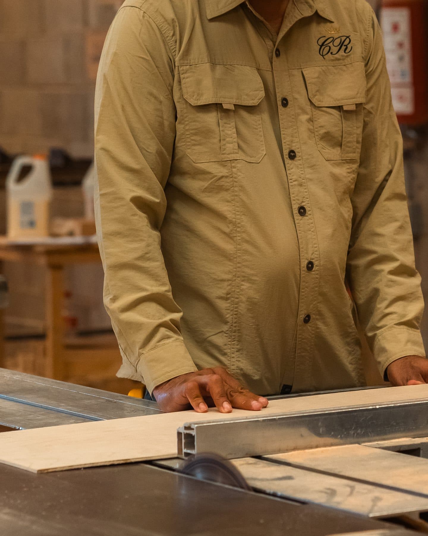 Craftsman in a Cristo Rey work shirt guiding a board through the table saw