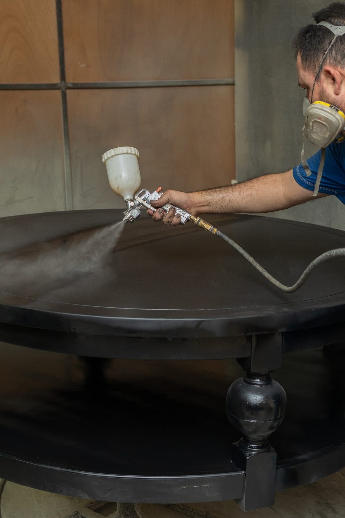 Craftsman spray-finishing a round Paris coffee table in the workshop
