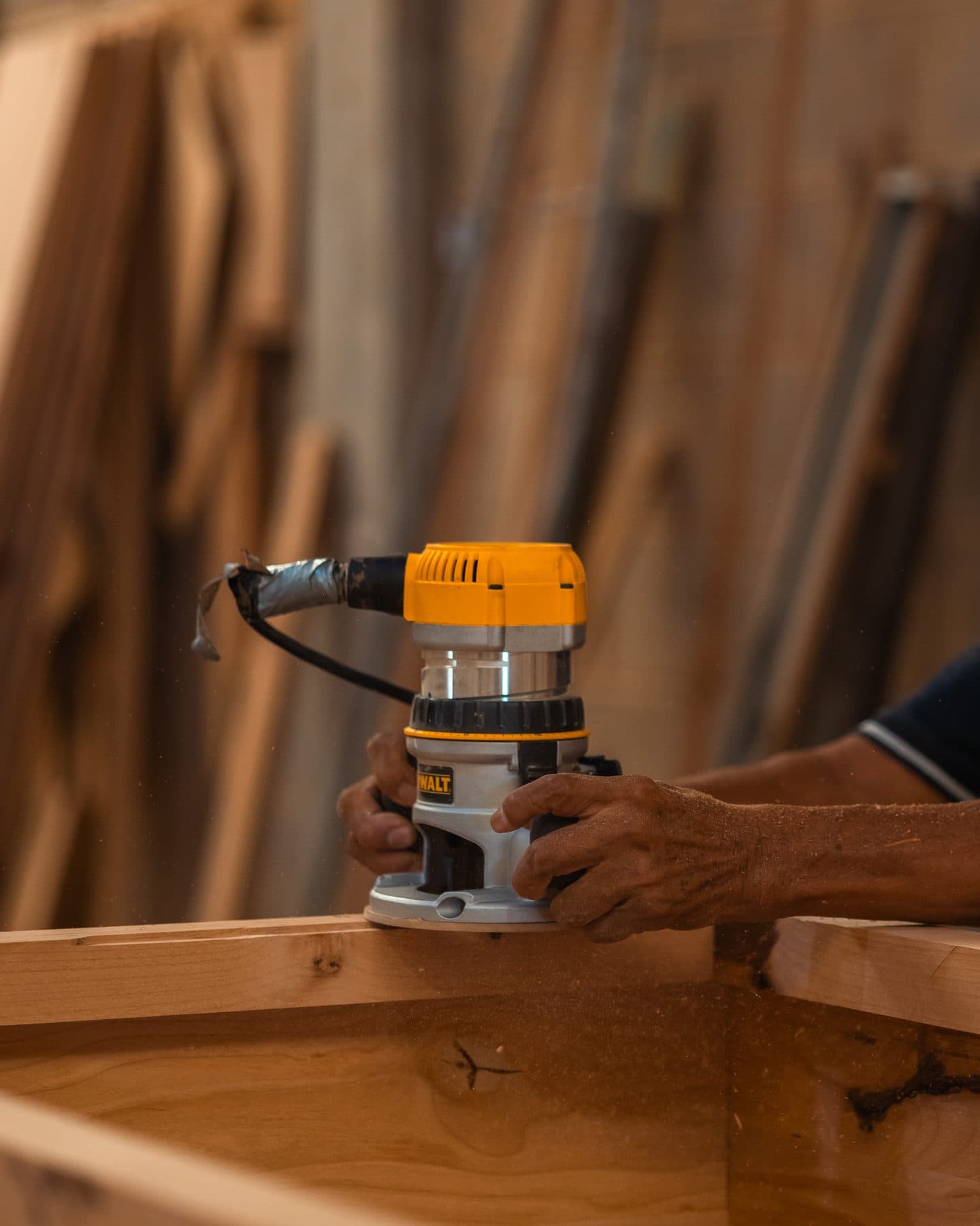 Hands guiding a router along the edge of a solid-wood frame